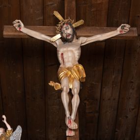 Zdjęcie nr 1: Pełnoplastyczna figura Chrystusa przybita do krzyża trzema gwoździami. Postać ukazana w łagodnym zwisie, ramiona ułożone w kształt litery „Y”, dłonie o lekko zaciśniętych palcach. Głowa, przechylona na prawą stronę, nogi skrzyżowane z prawą stopą założoną na lewą. Sylwetka ciała mocno wychudzona, z wydatną, wysuniętą do przodu klatką piersiową i wciętą talią. Twarz pociągła o wyrazistych rysach, okolona krótką brodą. Oczy o opadłych kącikach, usta rozchylone. Wokół bioder krótkie perizonium z fałdą przechodzącą między udami i zawiniętą z tyłu prawej nogi. Na głowie korona cierniowa, a wokół nimb krzyżowy. Karnacja ciała pokryta polichromią w naturalnym jasnokremowym odcieniu z zaznaczonymi śladami męki na dłoniach, stopach, prawym boku i czole. Perizonium, promienie w nimbie i korona cierniowa złote.