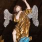 Zdjęcie nr 1: Pełnoplastyczna figura uskrzydlonego anioła ustawiona na niskim prostopadłościennym cokole. Anioł ukazany frontalnie na niebieskiej chmurze o silnie, esowato wygiętej sylwetce z głową uniesioną do góry, z prawą ręką złożoną na piersi, lewą ugiętą w łokciu uniesioną do góry. Twarz owalna o pełnych policzkach z drobnymi ustami i wyraźnie zaznaczonym podbródkiem. Włosy średniej długości, bujne, brązowe, zasłaniające uszy. Ubrany jest w złoconą tunikę z rękawami podwiniętymi do wysokości łokci, odsłaniającą prawą nogę. Polichromia w odsłoniętych partiach ciała naturalistyczna, skrzydła  srebrzone, suknia złocona, cokół i chmura malowane na niebiesko.