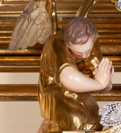 Zdjęcie nr 3: Pełnoplastyczne figury dwóch uskrzydlonych aniołów. Anioły zwrócone ku tabernakulum, ukazane w postawie klęczącej, z głową pochyloną delikatnie do przodu, z rękami ugiętymi w łokciach i wysuniętymi do przodu, które składają w geście modlitwy. Twarze podłużne o pełnych policzkach, z długimi nosami i dużymi niebieskimi oczami. Włosy krótkie, brązowe, falowane, zasłaniające uszy. Ubrane są w długie suknie z rękawami podwiniętymi do wysokości łokcia, przewiązane w pasie sznurami. Polichromia w odsłoniętych partiach ciała naturalistyczna, końcówki skrzydeł srebrzone, suknia złocona.