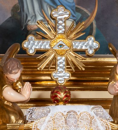 Zdjęcie nr 2: Pełnoplastyczne figury dwóch uskrzydlonych aniołów. Anioły zwrócone ku tabernakulum, ukazane w postawie klęczącej, z głową pochyloną delikatnie do przodu, z rękami ugiętymi w łokciach i wysuniętymi do przodu, które składają w geście modlitwy. Twarze podłużne o pełnych policzkach, z długimi nosami i dużymi niebieskimi oczami. Włosy krótkie, brązowe, falowane, zasłaniające uszy. Ubrane są w długie suknie z rękawami podwiniętymi do wysokości łokcia, przewiązane w pasie sznurami. Polichromia w odsłoniętych partiach ciała naturalistyczna, końcówki skrzydeł srebrzone, suknia złocona.