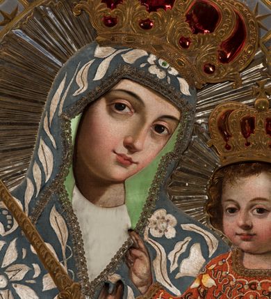 Zdjęcie nr 4: Obraz umieszczony jest w centralnej części południowego ołtarza, w prostokątnej niszy zamkniętej łukiem półkolistym. Ma kształt stojącego prostokąta, umieszczonego w profilowanej ramie. Przedstawia Matkę Boską z Dzieciątkiem siedzącym na jej ramieniu. Maria ukazana jest frontalnie, do pasa, z lekko pochyloną w lewo głową i berłem w prawej dłoni. Jej twarz jest owalna, o wyrazistych rysach, oczy duże, o wykroju migdałowym, ponad nimi brwi zarysowane gładkim łukiem. Nos prosty, usta pełne, ale niewielkie. Cera jasna, lekko zaróżowiona na policzkach. Madonna ubrana jest w biało-czerwoną haftowaną suknię i błękitny płaszcz zarzucony na głowę, pokryty motywami białych kwiatów i liści. Jezusa, którego okrągłą, pełną twarz okalają ułożone w miękkie fale włosy koloru brązowego, wyróżniają duże, migdałowe oczy, niewielki nos i drobne usta. Jest ubrany w pomarańczową suknię, na której wyhaftowane są biało-żółte kwiaty i wijące się brązowe wstęgi. Dzieciątko unosi prawą rączkę w geście błogosławieństwa, lewą dotyka dłoni matki. Na głowach Marii i Jezusa znajdują się zamknięte korony zwieńczone krzyżem, a wokół nich wytłaczane, srebrzyste nimby promieniste. Tło obrazu wykonane jest z metalowej blachy, zdobione srebrną kratką ułożoną pod kątem, ze złotymi gwiazdkami i rozetami w polach.
