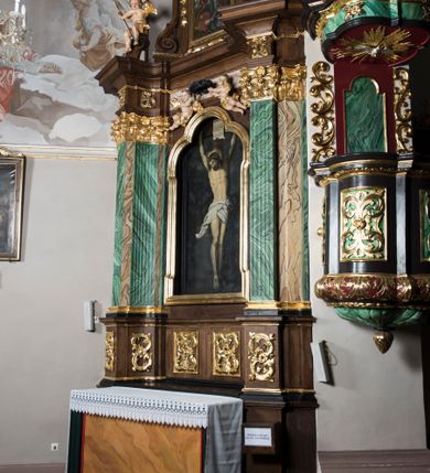 Zdjęcie nr 2: Ołtarz boczny, ustawiony w północno-wschodnim narożu korpus, jest architektoniczny, jednokondygnacyjny, jednoosiowy ze zwieńczeniem. Sam ołtarz z prostą mensą jest prostopadłościenny. Retabulum zostało zbudowane na zdwojonym cokole, ustawionym ukośnie, z filarami opiętymi z trzech stron pilastrami kompozytowymi podtrzymującymi belkowanie o znacznie wysuniętym gzymsie. Zwieńczenie jest w kształcie stojącego prostokąta ujętego ukośnie dostawionymi spływami wolutowymi dźwigającymi odcinki belkowania z silnie wyłamanym ku przodowi gzymsem z muszlą palmetową pośrodku. Na cokołach i w partii fryzu znajdują się wstęgi ornamentu regencyjnego z listkami i rozetami, a w zwieńczeniu kampanule podwieszone pod listkami akantu. W części środkowej wnęka ujęta w profilowaną ramę, prostokątną, z uszkami u dołu, zakończoną trójliściem, w której jest umieszczony obraz Chrystusa na krzyżu (na zasuwie obraz św. Antoniego Padewskiego); nad ramą para uskrzydlonych aniołków podtrzymujących koronę cierniową. Na belkowaniu siedzą uskrzydlone aniołki, przepasane opaską na biodrach, z narzędziami Męki Pańskiej w rękach. W zwieńczeniu o formie prostokąta zamkniętego łukiem półkolistym, nadwieszonym, w profilowanej ramie, znajduje się obraz ukazujący scenę z drogi krzyżowej – klęczącego Chrystusa pod krzyżem z Marią. Ołtarz polichromowany na ciemny brąz, z filarami i pilastrami imitującymi marmoryzację, ze złoconymi ornamentami i profilami; figury aniołów z naturalną karnacją, ze złoconymi skrzydłami. Polichromia ołtarza w tonacji brązowej i zielonej ze złoceniami. 

