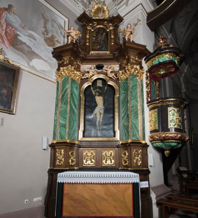 Zdjęcie nr 1: Ołtarz boczny, ustawiony w północno-wschodnim narożu korpus, jest architektoniczny, jednokondygnacyjny, jednoosiowy ze zwieńczeniem. Sam ołtarz z prostą mensą jest prostopadłościenny. Retabulum zostało zbudowane na zdwojonym cokole, ustawionym ukośnie, z filarami opiętymi z trzech stron pilastrami kompozytowymi podtrzymującymi belkowanie o znacznie wysuniętym gzymsie. Zwieńczenie jest w kształcie stojącego prostokąta ujętego ukośnie dostawionymi spływami wolutowymi dźwigającymi odcinki belkowania z silnie wyłamanym ku przodowi gzymsem z muszlą palmetową pośrodku. Na cokołach i w partii fryzu znajdują się wstęgi ornamentu regencyjnego z listkami i rozetami, a w zwieńczeniu kampanule podwieszone pod listkami akantu. W części środkowej wnęka ujęta w profilowaną ramę, prostokątną, z uszkami u dołu, zakończoną trójliściem, w której jest umieszczony obraz Chrystusa na krzyżu (na zasuwie obraz św. Antoniego Padewskiego); nad ramą para uskrzydlonych aniołków podtrzymujących koronę cierniową. Na belkowaniu siedzą uskrzydlone aniołki, przepasane opaską na biodrach, z narzędziami Męki Pańskiej w rękach. W zwieńczeniu o formie prostokąta zamkniętego łukiem półkolistym, nadwieszonym, w profilowanej ramie, znajduje się obraz ukazujący scenę z drogi krzyżowej – klęczącego Chrystusa pod krzyżem z Marią. Ołtarz polichromowany na ciemny brąz, z filarami i pilastrami imitującymi marmoryzację, ze złoconymi ornamentami i profilami; figury aniołów z naturalną karnacją, ze złoconymi skrzydłami. Polichromia ołtarza w tonacji brązowej i zielonej ze złoceniami. 

