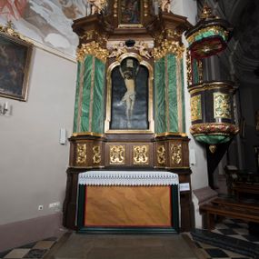 Zdjęcie nr 1: Ołtarz boczny, ustawiony w północno-wschodnim narożu korpus, jest architektoniczny, jednokondygnacyjny, jednoosiowy ze zwieńczeniem. Sam ołtarz z prostą mensą jest prostopadłościenny. Retabulum zostało zbudowane na zdwojonym cokole, ustawionym ukośnie, z filarami opiętymi z trzech stron pilastrami kompozytowymi podtrzymującymi belkowanie o znacznie wysuniętym gzymsie. Zwieńczenie jest w kształcie stojącego prostokąta ujętego ukośnie dostawionymi spływami wolutowymi dźwigającymi odcinki belkowania z silnie wyłamanym ku przodowi gzymsem z muszlą palmetową pośrodku. Na cokołach i w partii fryzu znajdują się wstęgi ornamentu regencyjnego z listkami i rozetami, a w zwieńczeniu kampanule podwieszone pod listkami akantu. W części środkowej wnęka ujęta w profilowaną ramę, prostokątną, z uszkami u dołu, zakończoną trójliściem, w której jest umieszczony obraz Chrystusa na krzyżu (na zasuwie obraz św. Antoniego Padewskiego); nad ramą para uskrzydlonych aniołków podtrzymujących koronę cierniową. Na belkowaniu siedzą uskrzydlone aniołki, przepasane opaską na biodrach, z narzędziami Męki Pańskiej w rękach. W zwieńczeniu o formie prostokąta zamkniętego łukiem półkolistym, nadwieszonym, w profilowanej ramie, znajduje się obraz ukazujący scenę z drogi krzyżowej – klęczącego Chrystusa pod krzyżem z Marią. Ołtarz polichromowany na ciemny brąz, z filarami i pilastrami imitującymi marmoryzację, ze złoconymi ornamentami i profilami; figury aniołów z naturalną karnacją, ze złoconymi skrzydłami. Polichromia ołtarza w tonacji brązowej i zielonej ze złoceniami. 


