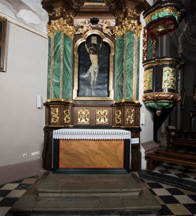 Zdjęcie nr 3: Ołtarz boczny, ustawiony w północno-wschodnim narożu korpus, jest architektoniczny, jednokondygnacyjny, jednoosiowy ze zwieńczeniem. Sam ołtarz z prostą mensą jest prostopadłościenny. Retabulum zostało zbudowane na zdwojonym cokole, ustawionym ukośnie, z filarami opiętymi z trzech stron pilastrami kompozytowymi podtrzymującymi belkowanie o znacznie wysuniętym gzymsie. Zwieńczenie jest w kształcie stojącego prostokąta ujętego ukośnie dostawionymi spływami wolutowymi dźwigającymi odcinki belkowania z silnie wyłamanym ku przodowi gzymsem z muszlą palmetową pośrodku. Na cokołach i w partii fryzu znajdują się wstęgi ornamentu regencyjnego z listkami i rozetami, a w zwieńczeniu kampanule podwieszone pod listkami akantu. W części środkowej wnęka ujęta w profilowaną ramę, prostokątną, z uszkami u dołu, zakończoną trójliściem, w której jest umieszczony obraz Chrystusa na krzyżu (na zasuwie obraz św. Antoniego Padewskiego); nad ramą para uskrzydlonych aniołków podtrzymujących koronę cierniową. Na belkowaniu siedzą uskrzydlone aniołki, przepasane opaską na biodrach, z narzędziami Męki Pańskiej w rękach. W zwieńczeniu o formie prostokąta zamkniętego łukiem półkolistym, nadwieszonym, w profilowanej ramie, znajduje się obraz ukazujący scenę z drogi krzyżowej – klęczącego Chrystusa pod krzyżem z Marią. Ołtarz polichromowany na ciemny brąz, z filarami i pilastrami imitującymi marmoryzację, ze złoconymi ornamentami i profilami; figury aniołów z naturalną karnacją, ze złoconymi skrzydłami. Polichromia ołtarza w tonacji brązowej i zielonej ze złoceniami. 

