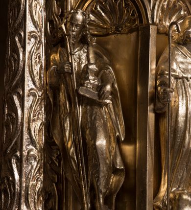 Zdjęcie nr 6: Tabernakulum w formie sześcianu, na niskim cokole, z dwukolumnowym portykiem utworzonym z pilastrów toskańskich i kolumn kompozytowych od frontu i dwóch analogicznych kolumn na tle pilastrów po bokach podtrzymujących przełamujące się na nimi belkowanie. Kolumny osadzone na niskich piedestałach, lekko wybrzuszonych, otoczonych liśćmi akantu. Kolumny pokryte symetrycznie układającymi i przeplatającymi się wokół pionowego trzpienia liśćmi i zwieńczone jońskimi kapitelami. Fryz belkowania zdobiony uskrzydloną główką aniołka, liściastymi wolutami, rautami w drobnych kartuszach i kostkowaniem. Drzwi tabernakulum zdobione są płaskorzeźbionym kielichem z hostią. Po bokach wypukło rzeźbione główki anielskie, a nad nimi okrągły medalion z literami IHS obwiedziony wieńcem laurowym, z elementami przechodzących między sobą listw kartuszowych i podwieszonych pod nie festonów. W ściankach naroży tabernakulum cztery nisze konchowe z muszlami wypełnione figurkami świętych. Jeden w wielbłądziej skórze trzymający księgę z barankiem przedstawia św. Jana Chrzciciela. Trzej pozostali są trudni do identyfikacji. Jeden trzyma otwartą księgę, a u jego stóp widnieje mitra książęca, drugi trzyma pastorał a u jego stóp leży infuła, trzeci z laską i kapeluszem u stóp (św. Jakub?). 


