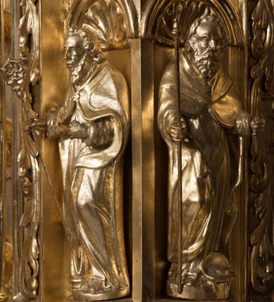 Zdjęcie nr 8: Tabernakulum w formie sześcianu, na niskim cokole, z dwukolumnowym portykiem utworzonym z pilastrów toskańskich i kolumn kompozytowych od frontu i dwóch analogicznych kolumn na tle pilastrów po bokach podtrzymujących przełamujące się na nimi belkowanie. Kolumny osadzone na niskich piedestałach, lekko wybrzuszonych, otoczonych liśćmi akantu. Kolumny pokryte symetrycznie układającymi i przeplatającymi się wokół pionowego trzpienia liśćmi i zwieńczone jońskimi kapitelami. Fryz belkowania zdobiony uskrzydloną główką aniołka, liściastymi wolutami, rautami w drobnych kartuszach i kostkowaniem. Drzwi tabernakulum zdobione są płaskorzeźbionym kielichem z hostią. Po bokach wypukło rzeźbione główki anielskie, a nad nimi okrągły medalion z literami IHS obwiedziony wieńcem laurowym, z elementami przechodzących między sobą listw kartuszowych i podwieszonych pod nie festonów. W ściankach naroży tabernakulum cztery nisze konchowe z muszlami wypełnione figurkami świętych. Jeden w wielbłądziej skórze trzymający księgę z barankiem przedstawia św. Jana Chrzciciela. Trzej pozostali są trudni do identyfikacji. Jeden trzyma otwartą księgę, a u jego stóp widnieje mitra książęca, drugi trzyma pastorał a u jego stóp leży infuła, trzeci z laską i kapeluszem u stóp (św. Jakub?). 


