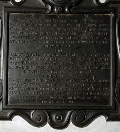 Zdjęcie nr 1: Tablica epitafijna w formie zbliżonej do kwadratu, w profilowanym obramieniu z uszakami przechodzącymi w spływy wolutowe. Nad płytą kartusz wokół owalnego, wypukłego pola z godłem herbu Dołęga. Pod płytą woluty stykają się z fartuchem. Na tablicy inskrypcja: „D(EO) O(PTIMO) M(AXIMO) / ET MAGNAE DEI MATRI HONOR AETERNVS. / PYS MANIBV(S) LONGA FELICITAS MARTINI DOBRVCHOWSKI, / CVIVS FLORE[M] AETATIS SOCIETAS IESV PER OMNES BONA/RV(M) ARTIV(M) DISCIPLINAS PIE AC FELICITER EXCOLVIT; / IVVENTVTE(M) SIGNA IMPERATORIA MAGNI EXCERCITVV(M) DVCIS / STANISLAI ZOŁKIEVII IDONEAM REBVS GERENDIS / FIRMAVERVNT. / HINC / RELIQVV(M) AETATIS ROBVR IN AVLA(M) MARTINI SZYSZKOVII: / EP(ISCOP)I CRACOVIEN(SIS). VIRIS ILLVSTRIB(US) FERACE(M) INTVLIT. / A QVO PRAEFECTVRA WAWRZYNECENSI ORNATVS EPI/SCOPALIS IN PAVPERES, ET SACROS HOMINES LIBERA/LITATIS LVCVLENTVS FVIT TESTIS, / AC FIDVS HAERES / CV(M) ET IPSE MVNIFICVS EIVS VIRTVTIS CVLTOR DE PRO/PRYS FORTVNAE BONIS PER OMNEM VITA(M) ESSET; / ANTIQVI MORIS, ET PLVRIMIS CONSPICVVS VIRTVTIBVS, / OBYT ANNO D(OMI)NI. 1640. MENSE IVNIO DIE 24 / AETATIS 5O. INGENTI OMNIBVS RELICTO / DESIDERIO SVI”.