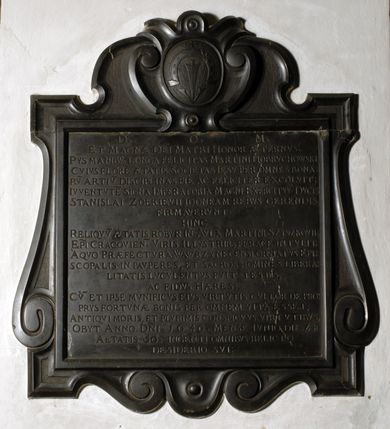 Zdjęcie nr 2: Tablica epitafijna w formie zbliżonej do kwadratu, w profilowanym obramieniu z uszakami przechodzącymi w spływy wolutowe. Nad płytą kartusz wokół owalnego, wypukłego pola z godłem herbu Dołęga. Pod płytą woluty stykają się z fartuchem. Na tablicy inskrypcja: „D(EO) O(PTIMO) M(AXIMO) / ET MAGNAE DEI MATRI HONOR AETERNVS. / PYS MANIBV(S) LONGA FELICITAS MARTINI DOBRVCHOWSKI, / CVIVS FLORE[M] AETATIS SOCIETAS IESV PER OMNES BONA/RV(M) ARTIV(M) DISCIPLINAS PIE AC FELICITER EXCOLVIT; / IVVENTVTE(M) SIGNA IMPERATORIA MAGNI EXCERCITVV(M) DVCIS / STANISLAI ZOŁKIEVII IDONEAM REBVS GERENDIS / FIRMAVERVNT. / HINC / RELIQVV(M) AETATIS ROBVR IN AVLA(M) MARTINI SZYSZKOVII: / EP(ISCOP)I CRACOVIEN(SIS). VIRIS ILLVSTRIB(US) FERACE(M) INTVLIT. / A QVO PRAEFECTVRA WAWRZYNECENSI ORNATVS EPI/SCOPALIS IN PAVPERES, ET SACROS HOMINES LIBERA/LITATIS LVCVLENTVS FVIT TESTIS, / AC FIDVS HAERES / CV(M) ET IPSE MVNIFICVS EIVS VIRTVTIS CVLTOR DE PRO/PRYS FORTVNAE BONIS PER OMNEM VITA(M) ESSET; / ANTIQVI MORIS, ET PLVRIMIS CONSPICVVS VIRTVTIBVS, / OBYT ANNO D(OMI)NI. 1640. MENSE IVNIO DIE 24 / AETATIS 5O. INGENTI OMNIBVS RELICTO / DESIDERIO SVI”.