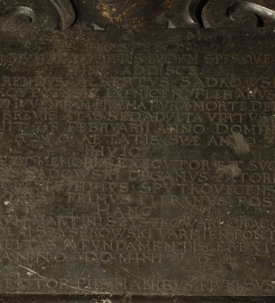 Zdjęcie nr 6: Tablica epitafijna w kształcie zbliżonym do kwadratu ujęta uszakami przechodzącymi w spływy wolutowe. Nad tablicą kartusz z godłem herbu Tępa Podkowa (wg Chrząńskiego odmiana typu c) i syglami A[LBERTUS] S[ADKOWSKI] P[LEBANUS] S[PYTKOVECENSIS] L[YPNICENSIS], zwieńczony krzyżem. Pod tablicą tarcza herbowa z godłem herbu Gozdawa i syglami I[OSEPHUS] S[ADKOWSKI] D[ECANVS] Z[ATORIENSIS] P[LEBANUS] S[PYTKOVeCENSIS]. Na tablicy inskrypcja: "D[EO] O[PTIMO] M[AXIMO] / HOSPES / LEVEM HVMANAE FORTIS LVDVM SPESQVE FALSAS / HINC ADDISCE. / REVERENDVS ALBERTUS SADKOWSKI / SPYTKOVECENSIS LYPNICEN(IS) PLEBANVS QVI / SENILEM IVVENTAM PRAEMATVRA MORTE DEPOSVIT / IN QVO BREVIS AETAS SED ADVLTA VIRTVS FVIT / OBIIT 28 FEBRVARII ANNO DOMINI / 1640 AETATIS SVA ANNO 31 / HVIC / AMORIS ET MEMORIAE EXECVTOR ET SVCCESSOR / JOSEPHVS SADOWSKI DECANVS ZATORIENSIS / ECCLESIAE HVIVS SPYTKOVECENSIS / QVAM VIDES PRIMVS PLEBANVS POSVIT / HANC / ILL(USTRISI)MORUM MARTINI SZYSZKOWSKI CRACOVIEN[SIS] ET NICOLAI SZYSZKOWSKI VARMIEN[SIS] PONTIFICVM / LIBERALITAS A FVNDAMENTIS EREXIT / ANNO DOMINI 1646 / ADDE LECTOR PIIS MANIBVS PIVM SVSPIRIVM".

