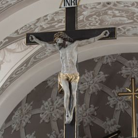 Zdjęcie nr 1: Na belce tęczowej o zarysie łuku wklęsło-wypukłego z uskokiem usytuowano krzyż z figurą Chrystusa i figury Marii i św. Jana Ewangelisty. Chrystus został przedstawiony frontalnie, w lekkim zwisie, z głową na wysokości dłoni, z nogami lekko ugiętymi w kolanach, skrzyżowanymi stopami, prawa na lewej, przybitymi do krzyża jednym gwoździem. Ręce rozłożone szeroko na ramionach krzyża, dłonie z lekko zgiętymi palcami są przebite gwoździami. Sylwetka Chrystusa jest delikatnie wygięta, głowa bezwładnie opada na prawe ramię. Jego twarz jest pociągła, nos prosty, wąski, oczy małe, zamknięte. Twarz okala szpiczasta, brązowa, krótka broda. Głowę przykrywają gęste, ciemne włosy o falistych, długich puklach zakrywające ucho i opadające na szyję oraz złota korona cierniowa. Ciało opracowane poprawnie pod względem anatomii, ale modelowane delikatnie, z lekko zarysowaną muskulaturą. Na biodrach krótkie perizonium, ze swobodnie opadającym wzdłuż prawego uda końcem materiału. W prawym boku Chrystusa widoczna jest rana od włóczni, z której wypływa krew, podobnie, jak z ran powstałych przez koronę cierniową, czy w miejscach przebitych gwoździami. Belka łuku tęczowego w kolorze brązowym, z fragmentami profilowania złoconymi. Rzeźba Chrystusa polichromowana naturalistycznie, ze złoconym perizonium oraz koroną cierniową i czerwonymi strużkami krwi.