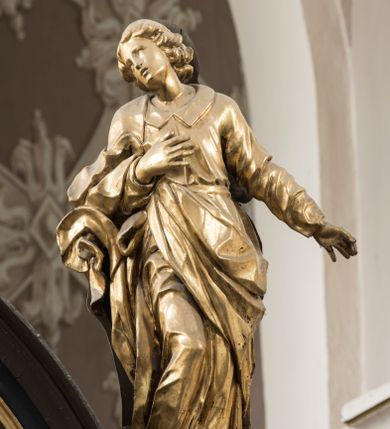 Zdjęcie nr 2: Święty po prawej stronie krzyża, ukazany w pozycji stojącej, w lekkim kontrapoście z ugiętą prawą nogą w kolanie, z głową i górną partią tułowia zwróconą w stronę Ukrzyżowanego, a dolną częścią ciała ukazaną niemal frontalnie. Głowa świętego ukazana w trzech czwartych, lekko przegięta na bok, zwraca się w stronę krzyża. Twarz smukła, z wydatnym podbródkiem i drobnymi ustami lekko rozchylonymi. Mały, prosty, szeroki nos; otwarte, migdałowate oczy od góry zaznaczone delikatnie rysującymi się łukami brwiowymi. Kręcone włosy do ramion układają się w grube pukle, spływają na szyje i zakrywają uszy. Jego prawa ręka jest zgięta w łokciu, przylega do piersi, lewa jest opuszczona i odsunięta od tułowia, z rozłożoną dłonią. Święty Jan jest ubrany w tunikę z kołnierzem i wąskimi rękawami, przewiązaną w pasie i sięgającą do ziemi. Przez prawe ramię przerzucony jest płaszcz, przechodzący pod lewą ręką  z końcem zarzuconym na prawe przedramię. Szaty są mocno pofałdowane, dynamicznie skłębione pod prawą ręką. Rzeźba w całości złocona. Na jej plecach wtórnie dodana deska o obrysie postaci z malowaną wersją świętego widocznego od strony ołtarza głównego.