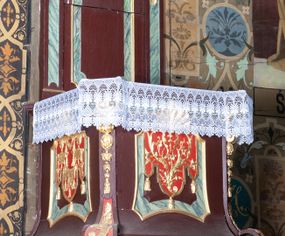 Zdjęcie nr 1: Ambona wisząca, przyścienna, z dostępem od zakrystii. Kosz na planie kwadratu o ściętych narożach, na cokole w formie wałka. U spodu podwieszony odwrócony, ścięty ostrosłup, o wklęsłych bokach, wydzielonych spływami wolutowymi dekorowanymi owocowymi festonami. Pola wypełnione ornamentem roślinnym. Całość zakończona szyszką w kształcie rozety z kulą. Ścianki kosza wydzielone pilastrami w formie wolut, spływających i ujmujących wypukłą cęgą ścięte naroża cokołu; trzony dekorowane owocowymi festonami oraz wstęgą przeplatającą się z ornamentem roślinnym. Podpory dźwigają parapet w formie gzymsu wyłamanego na ich osi. Na ściankach kwadratowe płyciny o wklęsłych narożach i dolnym boku, zwieńczone muszlą. W ich polach sztandary z trzema chwostami z płaskorzeźbioną dekoracją. Frontalny wypełniony wicią utworzoną ze strzępionych palmet i winnego grona; sztandar od strony prezbiterium z trzema obeliskami i podwieszonymi paludamentami w otoczeniu dekoracji roślinnej; sztandar od strony nawy z przedstawieniem trzech sztandarów oraz festonów z podwieszonej tkaniny.  Zaplecek w formie wydłużonego, stojącego prostokąta ujętego lizenami zakończonymi konsolami, dźwigającymi baldachim. Konsole dekorowane akantem z podwieszonymi festonami z tkaniny. W polu zaplecka prostokątna płycina o wklęsłych narożach, w której znajdują się drzwiczki. Baldachim na planie kwadratu o ściętych narożach, w formie niepełnego belkowania, wyłamanego w narożach. Fryz z trzech stron dekorowany kartuszami flankowanymi przez kwiatowe festony, z podwieszonym lambrekinem. U spodu z kwadratową płyciną o wklęsłych narożach. Belkowanie stanowi podstawię dla czterech wolutowych kabłąków podtrzymujących płomienisty wazon, z podwieszoną u spodu szyszką. Na zakończeniach wolut w narożach cztery wazony. 
Struktura polichromowana w kolorze brązowym z czerwonymi oraz marmoryzowanymi w kolorze jasnozielonym detalami; ornamentyka i ramki złocone.