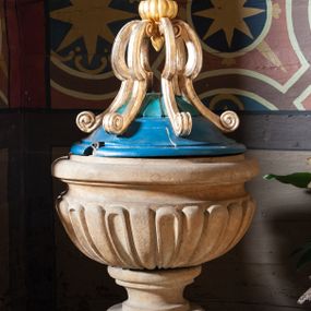 Zdjęcie nr 1: Chrzcielnica w typie kielichowym na płaskiej podstawie na planie koła, osadzona na niewysokim, ośmiobocznym postumencie. Stopa niewielka, ujęta półwałkiem. Spłaszczony, puklowany nodus trzonu ujęty parą talerzyków. Czara półkulistą o powierzchni imitującej puklowanie z wklęską i zaoblonym brzegiem. Stożkowata pokrywa zwieńczona sześcioma kabłąkami w formie spływów wolutowych, spiętymi ujętą dołem sterczynką zamkniętą kulą z krzyżem. Struktura kielicha chrzcielnicy utrzymana w kolorze kamienia, pokrywa polichromowana w kolorze niebieskim i turkusowym, zwieńczenie złocono-srebrzone.  