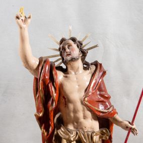 Zdjęcie nr 1: Rzeźba całopostaciowa, pełnoplastyczna, ustawiona na cokole w formie obłoku. Sylwetka Jezusa zwrócona na wprost, w wydatnym kontrapoście, z prawą nogą wspartą na leżącej na podstawie czaszce. Głowa Jezusa uniesiona, skierowana delikatnie w prawo. Twarz pociągła, o kwadratowym zarysie szczęki, o głęboko osadzonych oczach z drążonymi kącikami, zwróconych ku górze; prostym, długim nosie, rozchylonych ustach; okolona krótką kręconą brodą, układającą się w dwa pukle. Włosy długie, gęste, kręcone, układające się w wijące pasma, opadające na ramiona. Jezus w lewej ręce trzyma czerwony sztandar na drzewcu zakończonym krzyżem, prawą unosi wysoko w geście błogosławieństwa. Ciało o delikatnie zarysowanej muskulaturze z zaznaczonymi śladami męki. W partii bioder przepasany złoconym perizonium przewiązanym sznurem, sięgającym połowy uda i odsłaniającym lewe biodro; tkanina drapowana w grube fałdy, marszczona, z wywiniętym brzegiem. Na ramiona narzucony czerwony płaszcz opadający na plecy, drapowany w proste fałdy, z zawiniętym brzegiem. Głowę ujmuje gloria promienista.