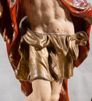 Zdjęcie nr 3: Rzeźba całopostaciowa, pełnoplastyczna, ustawiona na cokole w formie obłoku. Sylwetka Jezusa zwrócona na wprost, w wydatnym kontrapoście, z prawą nogą wspartą na leżącej na podstawie czaszce. Głowa Jezusa uniesiona, skierowana delikatnie w prawo. Twarz pociągła, o kwadratowym zarysie szczęki, o głęboko osadzonych oczach z drążonymi kącikami, zwróconych ku górze; prostym, długim nosie, rozchylonych ustach; okolona krótką kręconą brodą, układającą się w dwa pukle. Włosy długie, gęste, kręcone, układające się w wijące pasma, opadające na ramiona. Jezus w lewej ręce trzyma czerwony sztandar na drzewcu zakończonym krzyżem, prawą unosi wysoko w geście błogosławieństwa. Ciało o delikatnie zarysowanej muskulaturze z zaznaczonymi śladami męki. W partii bioder przepasany złoconym perizonium przewiązanym sznurem, sięgającym połowy uda i odsłaniającym lewe biodro; tkanina drapowana w grube fałdy, marszczona, z wywiniętym brzegiem. Na ramiona narzucony czerwony płaszcz opadający na plecy, drapowany w proste fałdy, z zawiniętym brzegiem. Głowę ujmuje gloria promienista.