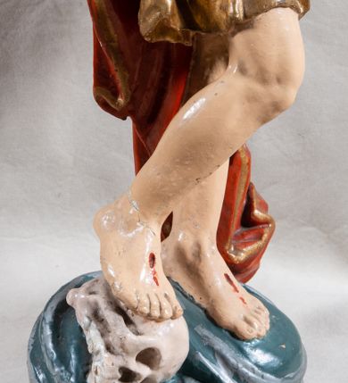 Zdjęcie nr 9: Rzeźba całopostaciowa, pełnoplastyczna, ustawiona na cokole w formie obłoku. Sylwetka Jezusa zwrócona na wprost, w wydatnym kontrapoście, z prawą nogą wspartą na leżącej na podstawie czaszce. Głowa Jezusa uniesiona, skierowana delikatnie w prawo. Twarz pociągła, o kwadratowym zarysie szczęki, o głęboko osadzonych oczach z drążonymi kącikami, zwróconych ku górze; prostym, długim nosie, rozchylonych ustach; okolona krótką kręconą brodą, układającą się w dwa pukle. Włosy długie, gęste, kręcone, układające się w wijące pasma, opadające na ramiona. Jezus w lewej ręce trzyma czerwony sztandar na drzewcu zakończonym krzyżem, prawą unosi wysoko w geście błogosławieństwa. Ciało o delikatnie zarysowanej muskulaturze z zaznaczonymi śladami męki. W partii bioder przepasany złoconym perizonium przewiązanym sznurem, sięgającym połowy uda i odsłaniającym lewe biodro; tkanina drapowana w grube fałdy, marszczona, z wywiniętym brzegiem. Na ramiona narzucony czerwony płaszcz opadający na plecy, drapowany w proste fałdy, z zawiniętym brzegiem. Głowę ujmuje gloria promienista.