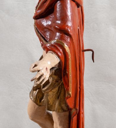 Zdjęcie nr 12: Rzeźba całopostaciowa, pełnoplastyczna, ustawiona na cokole w formie obłoku. Sylwetka Jezusa zwrócona na wprost, w wydatnym kontrapoście, z prawą nogą wspartą na leżącej na podstawie czaszce. Głowa Jezusa uniesiona, skierowana delikatnie w prawo. Twarz pociągła, o kwadratowym zarysie szczęki, o głęboko osadzonych oczach z drążonymi kącikami, zwróconych ku górze; prostym, długim nosie, rozchylonych ustach; okolona krótką kręconą brodą, układającą się w dwa pukle. Włosy długie, gęste, kręcone, układające się w wijące pasma, opadające na ramiona. Jezus w lewej ręce trzyma czerwony sztandar na drzewcu zakończonym krzyżem, prawą unosi wysoko w geście błogosławieństwa. Ciało o delikatnie zarysowanej muskulaturze z zaznaczonymi śladami męki. W partii bioder przepasany złoconym perizonium przewiązanym sznurem, sięgającym połowy uda i odsłaniającym lewe biodro; tkanina drapowana w grube fałdy, marszczona, z wywiniętym brzegiem. Na ramiona narzucony czerwony płaszcz opadający na plecy, drapowany w proste fałdy, z zawiniętym brzegiem. Głowę ujmuje gloria promienista.