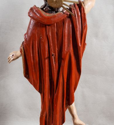 Zdjęcie nr 11: Rzeźba całopostaciowa, pełnoplastyczna, ustawiona na cokole w formie obłoku. Sylwetka Jezusa zwrócona na wprost, w wydatnym kontrapoście, z prawą nogą wspartą na leżącej na podstawie czaszce. Głowa Jezusa uniesiona, skierowana delikatnie w prawo. Twarz pociągła, o kwadratowym zarysie szczęki, o głęboko osadzonych oczach z drążonymi kącikami, zwróconych ku górze; prostym, długim nosie, rozchylonych ustach; okolona krótką kręconą brodą, układającą się w dwa pukle. Włosy długie, gęste, kręcone, układające się w wijące pasma, opadające na ramiona. Jezus w lewej ręce trzyma czerwony sztandar na drzewcu zakończonym krzyżem, prawą unosi wysoko w geście błogosławieństwa. Ciało o delikatnie zarysowanej muskulaturze z zaznaczonymi śladami męki. W partii bioder przepasany złoconym perizonium przewiązanym sznurem, sięgającym połowy uda i odsłaniającym lewe biodro; tkanina drapowana w grube fałdy, marszczona, z wywiniętym brzegiem. Na ramiona narzucony czerwony płaszcz opadający na plecy, drapowany w proste fałdy, z zawiniętym brzegiem. Głowę ujmuje gloria promienista.