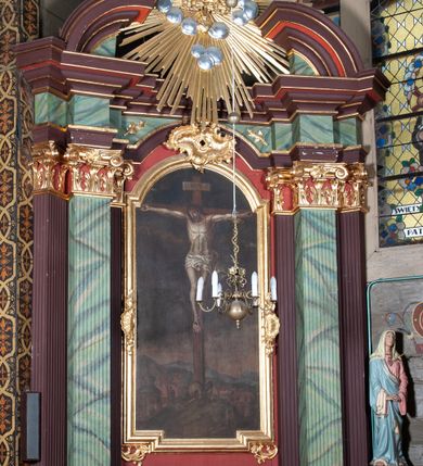 Zdjęcie nr 1: Ołtarz przyścienny, architektoniczny, z mensą w formie sarkofagu, dwustrefową, o wklęsło-wypukłych bokach. Mensa z kamiennym portatylem. Retabulum jednoosiowe, jednokondygnacyjne, ustawione na wysokim cokole, ujęte parą półfilarów kompozytowych o kanelowanych trzonach ustawionych na tle podwójnych pilastrów, z których zewnętrzne dostawione ukośnie. Podpory wspierają wyłamujące się belkowanie z architrawem wygiętym w  łuk nadwieszony nad polem środkowym i wydatnym, profilowanym gzymsem.  W zwieńczeniu przerwany, półkolisty przyczółek oraz gloria promienista z obłokami, pośrodku których aplikowany hierogram IHS. 
W polu środkowym wycięta wnęka ujęta profilowaną ramą, w kształcie stojącego prostokąta, zamkniętego łukiem nadwieszonym. We wnęce obraz z przedstawieniem  Ukrzyżowania Chrystusa, nad którym rzeźbiony kartusz formowany z ornamentu rocaille&#039;owego.
Całość struktury ołtarza malowana w kolorze ciemnobrązowym, Półfilary, fryz oraz mensa pokryte malowaną marmoryzacją w odcieniach zieleni, pole środkowe ciemnoczerwone, detal architektoniczny  i profilowania pozłacane.