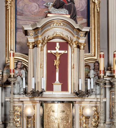 Zdjęcie nr 26: Ołtarz architektoniczny, jednoosiowy z bramkami, jednokondygnacyjny ze zwieńczeniem, na podwójnym cokole. Ołtarz murowany, licowany kamiennymi płytami, prostopadłościenny. Mensa betonowa. Antependium w formie wydłużonego, leżącego prostokąta, ujętego profilowaną ramą. Na srebrzonym polu płaskorzeźbiona, złocona dekoracja; w centrum rocaillowy kartusz ze sceną Zwiastowania Najświętszej Marii Panny, flankowany parą rocaillowych płycin, w których prawa z przedstawieniem mitry książęcej na poduszce ujętej różanymi gałązkami z gwiazdą, lewa z berłem na poduszce ujętym liliami zwieńczonej słońcem. 
Tabernaculum w formie prostopadłościennej szafki o wypukłej ścianie frontowej, z dwuskrzydłowymi drzwiczkami o kształcie zbliżonym do kwadratu, ujęte ramą; na łączeniu drzwiczek krzyż, flankowany przez odlewane kłosy zbóż i winne grono, całość na fakturowanym tle. Tabernaculum w drewnianej obudowie stanowiącej podstawę dla tronu wystawienia; cokół wyłamany, dekorowany płycinami z ornamentem roślinnym i campanullami; całość zamknięta gzymsem. Tron wystawienia w formie aediculi z obrotową niszą; ujęte parą półkolumn i parą kolumn o kapitelach kompozytowych i pseudokanelowanych trzonach dźwigających pełne belkowanie, wypukłe i wyłamane na kształt łuku odcinkowego nad niszą, wyłamane na osiach podpór. Nisza ujęta opaską dekorowaną akantem. W partii fryzu rozety i dekoracja roślinna. Całość zwieńczona postumentem  z leżącym na księdze barankiem. Tron flankują dwie figurki, adorujących aniołków, klęczących na cokole.
Nastawa ołtarzowa ujęta trzema parami pilastrów i parą skrajnych filarów o kapitelach kompozytowych i kanelowanych trzonach; oraz stojących przed nimi w dwóch strefach dwiema parami kolumn o kapitelach kompozytowych. Podpory dźwigają pełne belkowanie, wyłamane na ich osi; nad polem środkowym architraw przyjmuje kształt łuku nadwieszonego. Belkowanie oraz cokoły kolumn ustawione delikatnie pod katem względem lica retabulum. Na belkowaniu, na osi skrajnych kolumn przerwany, wolutowy przyczółek z siedzącą parą puttów. W polu środkowym  nisza w formie stojącego prostokąta zamkniętego łukiem nadwieszonym, z wklęsłymi dolnymi narożami i dolnym bokiem; ujęta profilowaną ramą; w polu płaskorzeźbiona scena z Widzeniem św. Franciszka. Zwieńczenie w formie stojącego prostokąta ujętego lizenami oraz spływami wolutowymi; zamknięte gzymsem przechodzącym w dwie zwrócone antytetycznie woluty. W polu obraz w formie stojącego owalu w profilowanej ramie z przedstawieniem św. Michała Archanioła. Retabulum ujęte bramkami z przejściami w formie stojącego prostokąta zamkniętego łukiem nadwieszonym z uskokiem, z drzwiczkami; zwieńczone podtrzymywanym przez konsolę cokołem dla figur aniołów, flankowanym spływami wolutowymi.
Cokoły dla kolumn dekorowane z trzech stron płycinami. Rama obrazu pola środkowego zdobiona na bokach rocaille z kwiatami i palmami; łuk zwieńczony rocaillowym kartuszem, flankowanym przez dwie palmy. Na gzymsie nad polem środkowym muszla. Lizeny i woluty zwieńczenia dekorowane campanullami; obraz u spodu i u góry ujęty rocaille. Na gzymsie wieńczącym dwa kwiatowe festony; na jego skraju para wazonów, całość zwieńczona stylizowanym rokokowym krzyżem.
Struktura polichromowana w kolorze kremowym, z detalami w kolorach szarym i brudnym różem; trzony kolumn marmoryzowane; ornamentyka i profile złocone.