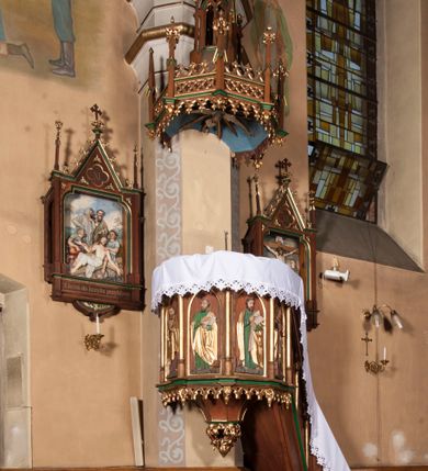 Zdjęcie nr 2: Ambona wisząca, przyścienna, składająca się z kosza, baldachimu i schodów z balustradą. Kosz na planie ośmioboku, podzielony na pola gładkimi, złoconymi kolumnami podtrzymującymi gzyms i parapet. W polach płyciny w formie stojącego prostokąta zamkniętego łukiem ostrym. W płycinach całopostaciowe figury ewangelistów – od strony schodów – św. Jan, św. Łukasz, św. Marek i św. Mateusz. Każdy z nich ubrany w długą suknię, z narzuconym złotym płaszczem, trzyma w rękach otwartą księgę i ma przy nodze właściwy atrybut. Wzdłuż ramy dolnej ażurowy ornament maswerkowy. Do podstawy podwieszona szyszka złożona z liści akantu. Baldachim na planie części ośmioboku o architektonicznym zwieńczeniu. Daszek zdobiony ażurowymi ornamentami maswerkowymi, z pinaklami zwieńczonymi kwiatonami na narożach. Szczyt w formie ażurowej wieży zwieńczonej kwiatonem. W podniebieniu baldachimu wyobrażenie gołębicy Ducha Świętego na tle glorii promienistej. Schody dostawione od strony wschodniej, dwukrotnie załamane, z czterema gładkimi płycinami oddzielonymi złoconymi kolumnami.