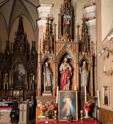 Zdjęcie nr 3: Ołtarz przyścienny, architektoniczny, trójosiowy, jednokondygnacyjny ze zwieńczeniem. Mensa skrzyniowa, prostopadłościenna. Antepedium z trzema prostokątnymi płycinami. W środkowej monogram IHS, boczne wypełnione symetrycznym ornamentem roślinnym. Predella wysoka, dekorowana fryzem arkadkowym, ostrołukowym. W pierwszej kondygnacji retabulum trzy nisze prostokątne zamknięte od góry wimpergą na tle szczytu. Środkowa nisza wyższa i szersza od bocznych, rama dekorowana wyschniętą wicią roślinną, wszystkie zdobione ażurowym ornamentem ostrołukowym i żabkami; szczyty wypełniają pola wypełnione łukiem trójlistnym, ostrym. Boczne nisze zwieńczone ustawionymi skośnie ażurowymi kapliczkami z pinaklami, zdobionymi żabkami i kwiatonami. W środkowej niszy figura Najświętszego Serca Jezusa, w bocznych św. Wojciech i św. Stanisław. W zwieńczeniu ażurowa kapliczka powtarzająca kształt kapliczek wieńczących osie boczne pierwszej kondygnacji z niszą, w której figura św. Antoniego Padewskiego. 
Struktura brązowa, niektóre detale malowane na zielono, ornamenty, profile i kolumny złocone. 
