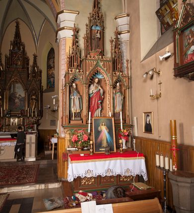 Zdjęcie nr 4: Ołtarz przyścienny, architektoniczny, trójosiowy, jednokondygnacyjny ze zwieńczeniem. Mensa skrzyniowa, prostopadłościenna. Antepedium z trzema prostokątnymi płycinami. W środkowej monogram IHS, boczne wypełnione symetrycznym ornamentem roślinnym. Predella wysoka, dekorowana fryzem arkadkowym, ostrołukowym. W pierwszej kondygnacji retabulum trzy nisze prostokątne zamknięte od góry wimpergą na tle szczytu. Środkowa nisza wyższa i szersza od bocznych, rama dekorowana wyschniętą wicią roślinną, wszystkie zdobione ażurowym ornamentem ostrołukowym i żabkami; szczyty wypełniają pola wypełnione łukiem trójlistnym, ostrym. Boczne nisze zwieńczone ustawionymi skośnie ażurowymi kapliczkami z pinaklami, zdobionymi żabkami i kwiatonami. W środkowej niszy figura Najświętszego Serca Jezusa, w bocznych św. Wojciech i św. Stanisław. W zwieńczeniu ażurowa kapliczka powtarzająca kształt kapliczek wieńczących osie boczne pierwszej kondygnacji z niszą, w której figura św. Antoniego Padewskiego. 
Struktura brązowa, niektóre detale malowane na zielono, ornamenty, profile i kolumny złocone. 
