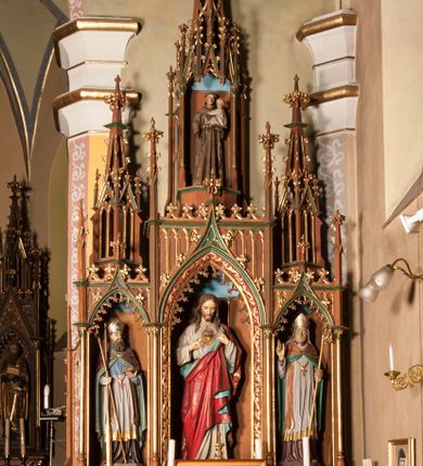 Zdjęcie nr 1: Ołtarz przyścienny, architektoniczny, trójosiowy, jednokondygnacyjny ze zwieńczeniem. Mensa skrzyniowa, prostopadłościenna. Antepedium z trzema prostokątnymi płycinami. W środkowej monogram IHS, boczne wypełnione symetrycznym ornamentem roślinnym. Predella wysoka, dekorowana fryzem arkadkowym, ostrołukowym. W pierwszej kondygnacji retabulum trzy nisze prostokątne zamknięte od góry wimpergą na tle szczytu. Środkowa nisza wyższa i szersza od bocznych, rama dekorowana wyschniętą wicią roślinną, wszystkie zdobione ażurowym ornamentem ostrołukowym i żabkami; szczyty wypełniają pola wypełnione łukiem trójlistnym, ostrym. Boczne nisze zwieńczone ustawionymi skośnie ażurowymi kapliczkami z pinaklami, zdobionymi żabkami i kwiatonami. W środkowej niszy figura Najświętszego Serca Jezusa, w bocznych św. Wojciech i św. Stanisław. W zwieńczeniu ażurowa kapliczka powtarzająca kształt kapliczek wieńczących osie boczne pierwszej kondygnacji z niszą, w której figura św. Antoniego Padewskiego. 
Struktura brązowa, niektóre detale malowane na zielono, ornamenty, profile i kolumny złocone. 
