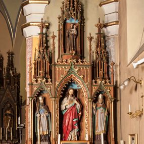 Zdjęcie nr 1: Ołtarz przyścienny, architektoniczny, trójosiowy, jednokondygnacyjny ze zwieńczeniem. Mensa skrzyniowa, prostopadłościenna. Antepedium z trzema prostokątnymi płycinami. W środkowej monogram IHS, boczne wypełnione symetrycznym ornamentem roślinnym. Predella wysoka, dekorowana fryzem arkadkowym, ostrołukowym. W pierwszej kondygnacji retabulum trzy nisze prostokątne zamknięte od góry wimpergą na tle szczytu. Środkowa nisza wyższa i szersza od bocznych, rama dekorowana wyschniętą wicią roślinną, wszystkie zdobione ażurowym ornamentem ostrołukowym i żabkami; szczyty wypełniają pola wypełnione łukiem trójlistnym, ostrym. Boczne nisze zwieńczone ustawionymi skośnie ażurowymi kapliczkami z pinaklami, zdobionymi żabkami i kwiatonami. W środkowej niszy figura Najświętszego Serca Jezusa, w bocznych św. Wojciech i św. Stanisław. W zwieńczeniu ażurowa kapliczka powtarzająca kształt kapliczek wieńczących osie boczne pierwszej kondygnacji z niszą, w której figura św. Antoniego Padewskiego. 
Struktura brązowa, niektóre detale malowane na zielono, ornamenty, profile i kolumny złocone. 
