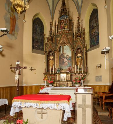 Zdjęcie nr 3: Nastawa ołtarzowa architektoniczna, trójosiowa, jednokondygnacyjna ze zwieńczeniem i predellą. Mensa skrzyniowa, prostopadłościenna. Antepedium z profilowaną płyciną, w centrum medalion z monogramem IHS i gorejącym sercem w glorii. Medalion ujęty profilowanymi płycinami o krawędziach wklęsłych od strony medaliony. Predella wysoka trójdzielna, boczne płyciny dekorowane fryzem arkadkowym ostrołukowym, przed środkową ustawione tabernakulum. W pierwszej kondygnacji retabulum trzy nisze prostokątne zamknięte od góry wimpergą. Środkowa nisza wyższa i szersza od bocznych, rama dekorowana astwerkiem, zwieńczenie łuku wypełnia ażurowy ornament ostrołukowy złączony gałązkami wyschniętej wici. Boczne nisze zdobione ażurowym ornamentem ostrołukowym i żabkami, szczyty wypełniają pola z łukiem trójlistnym ostrym oraz pas dekoracji z rombów wypełnionych motywem czteroliścia. Boczne nisze zwieńczone ustawionymi skośnie ażurowymi kapliczkami z pinaklami, zdobionymi żabkami i kwiatonami. W środkowej niszy obraz z przedstawieniem św. Anny z Marią i Jezusem, w bocznych figury św. Piotra i św. Pawła. W zwieńczeniu bardzo rozbudowana ażurowa kapliczka z niszą z rzeźbionym przedstawieniem Trójcy Świętej. Oprawa tabernakulum trójosiowa, na wysokim cokole zamkniętym wydatnym gzymsem oraz fryzem z astwerkiem; osie boczne cofnięte. Cokół dekorowany esownicami z akantem, boczne różami. Na osi środkowej tabernakulum o groszkowanych drzwiczkach w formie stojącego prostokąta z aplikowanymi kielichem z hostią oraz flankującą go winną latoroślą. Na osiach bocznych blendy z płaskorzeźbionym motywem roślinnym. 
Struktura brązowa, niektóre detale malowane na zielono, ornamenty, profile i kolumny złocone; mensa malowana na biało, ze złoconymi profilami. 