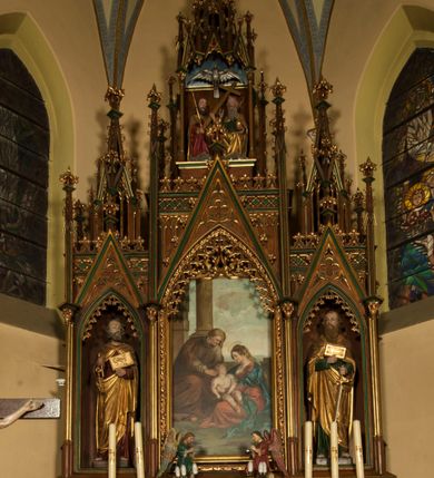 Zdjęcie nr 1: Nastawa ołtarzowa architektoniczna, trójosiowa, jednokondygnacyjna ze zwieńczeniem i predellą. Mensa skrzyniowa, prostopadłościenna. Antepedium z profilowaną płyciną, w centrum medalion z monogramem IHS i gorejącym sercem w glorii. Medalion ujęty profilowanymi płycinami o krawędziach wklęsłych od strony medaliony. Predella wysoka trójdzielna, boczne płyciny dekorowane fryzem arkadkowym ostrołukowym, przed środkową ustawione tabernakulum. W pierwszej kondygnacji retabulum trzy nisze prostokątne zamknięte od góry wimpergą. Środkowa nisza wyższa i szersza od bocznych, rama dekorowana astwerkiem, zwieńczenie łuku wypełnia ażurowy ornament ostrołukowy złączony gałązkami wyschniętej wici. Boczne nisze zdobione ażurowym ornamentem ostrołukowym i żabkami, szczyty wypełniają pola z łukiem trójlistnym ostrym oraz pas dekoracji z rombów wypełnionych motywem czteroliścia. Boczne nisze zwieńczone ustawionymi skośnie ażurowymi kapliczkami z pinaklami, zdobionymi żabkami i kwiatonami. W środkowej niszy obraz z przedstawieniem św. Anny z Marią i Jezusem, w bocznych figury św. Piotra i św. Pawła. W zwieńczeniu bardzo rozbudowana ażurowa kapliczka z niszą z rzeźbionym przedstawieniem Trójcy Świętej. Oprawa tabernakulum trójosiowa, na wysokim cokole zamkniętym wydatnym gzymsem oraz fryzem z astwerkiem; osie boczne cofnięte. Cokół dekorowany esownicami z akantem, boczne różami. Na osi środkowej tabernakulum o groszkowanych drzwiczkach w formie stojącego prostokąta z aplikowanymi kielichem z hostią oraz flankującą go winną latoroślą. Na osiach bocznych blendy z płaskorzeźbionym motywem roślinnym. 
Struktura brązowa, niektóre detale malowane na zielono, ornamenty, profile i kolumny złocone; mensa malowana na biało, ze złoconymi profilami. 