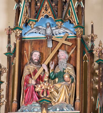 Zdjęcie nr 1: Grupa składa się z siedzących na obłokach postaci Boga Ojca i Jezusa, powyżej których wznosi się gołębica Ducha Świętego. Mężczyźni są zwróceni do siebie. Bóg zasiadający po prawej stronie ma wygląd starego mężczyzny, w lewej, wyciągniętej ręce trzyma jabłko królewskie, prawą unosi w geście błogosławieństwa. Ma owalną twarz okoloną siwymi włosami i długą, falowaną brodą, która opada mu na pierś. Jest ubrany w zieloną, przepasaną suknię oraz złoty płaszcz, który zakrywa mu ramiona i nogi. Jezus zasiadający po lewej stronie, w prawej ręce trzyma berło, lewą podtrzymuje krzyż. Ma pociągłą twarz o wyraźnych rysach, okoloną brązowym zarostem. Długie włosy opadają mu na ramiona i plecy. Jezus jest ubrany w czerwoną tunikę przepasaną w talii oraz złoty płaszcz spięty na piersi fibulą. Ponad figurami umieszczono srebrzoną postać gołębicy Ducha Świętego. W partiach ciała polichromia naturalistyczna, płaszcze i atrybuty złocone.