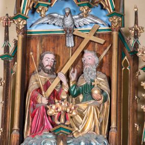 Zdjęcie nr 1: Grupa składa się z siedzących na obłokach postaci Boga Ojca i Jezusa, powyżej których wznosi się gołębica Ducha Świętego. Mężczyźni są zwróceni do siebie. Bóg zasiadający po prawej stronie ma wygląd starego mężczyzny, w lewej, wyciągniętej ręce trzyma jabłko królewskie, prawą unosi w geście błogosławieństwa. Ma owalną twarz okoloną siwymi włosami i długą, falowaną brodą, która opada mu na pierś. Jest ubrany w zieloną, przepasaną suknię oraz złoty płaszcz, który zakrywa mu ramiona i nogi. Jezus zasiadający po lewej stronie, w prawej ręce trzyma berło, lewą podtrzymuje krzyż. Ma pociągłą twarz o wyraźnych rysach, okoloną brązowym zarostem. Długie włosy opadają mu na ramiona i plecy. Jezus jest ubrany w czerwoną tunikę przepasaną w talii oraz złoty płaszcz spięty na piersi fibulą. Ponad figurami umieszczono srebrzoną postać gołębicy Ducha Świętego. W partiach ciała polichromia naturalistyczna, płaszcze i atrybuty złocone.