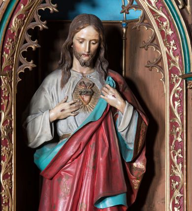 Zdjęcie nr 1: Rzeźba pełnoplastyczna przedstawiająca Chrystusa, stojącego centralnie, z prawą nogą lekko ugiętą w kolanie. Ręce z widocznymi znakami męki, odsłaniają spod szat gorejące serce. Głowa lekko pochylona, oczy skierowane w dół, nos prosty, usta wąskie. Na twarzy krótki brązowy zarost oraz włosy lekko pofalowane, opadające na ramiona. Chrystus jest ubrany w białą tunikę z długimi rękawami, odsłaniającą nagie stopy. Ma czerwony płaszcz, dekorowany złotym ornamentem, z niebieskim podszyciem, przerzucony przez lewe ramię, mocno sfałdowany.
Polichromia w partiach ciała naturalistyczna.