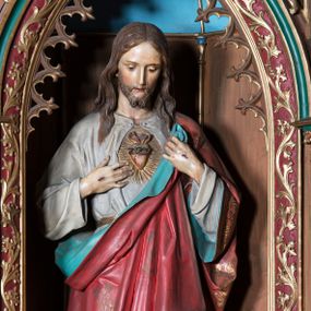 Zdjęcie nr 1: Rzeźba pełnoplastyczna przedstawiająca Chrystusa, stojącego centralnie, z prawą nogą lekko ugiętą w kolanie. Ręce z widocznymi znakami męki, odsłaniają spod szat gorejące serce. Głowa lekko pochylona, oczy skierowane w dół, nos prosty, usta wąskie. Na twarzy krótki brązowy zarost oraz włosy lekko pofalowane, opadające na ramiona. Chrystus jest ubrany w białą tunikę z długimi rękawami, odsłaniającą nagie stopy. Ma czerwony płaszcz, dekorowany złotym ornamentem, z niebieskim podszyciem, przerzucony przez lewe ramię, mocno sfałdowany.
Polichromia w partiach ciała naturalistyczna.