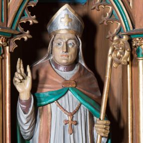 Zdjęcie nr 1: Rzeźba pełna na cokole przedstawiająca św. Stanisława stojącego frontalnie. Święty ma głowę zwróconą nieznacznie w prawo, wzrok skierowany przed siebie, nos prosty, usta wąskie;  na głowie ma infułę. Prawą rękę unosi w geście błogosławieństwa, lewą podtrzymuje złocony pastorał. Święty jest ubrany w brązową albę, białą komżę ze złoconą koronką u dołu, jasnobrązową stułę, ze złoconymi brzegami, złoty krzyż biskupi i jasnobrązowy płaszcz z zielonym podszyciem, spięty fibulą na piersi. Spod szat widoczne brązowe buty. 
Polichromia w partiach ciała naturalistyczna.
