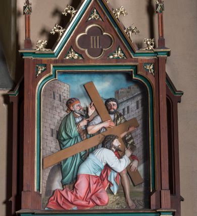Zdjęcie nr 3: Stacje drogi krzyżowej wkomponowane w rozbudowane, drewniane neogotyckie ramy o formach przypominających kapliczki, flankowane uszakami w kształcie przypór oraz zwieńczone parami pinakli i wimpergą dekorowaną żabkami i zakończoną kwiatonem z krzyżem. Wpisano w nie motyw czworoliścia otoczony trzema rozetkami. Od dołu dekoracyjne podwieszenie. Poszczególne przedstawienia umieszczone za szybą, ujętą w profilowane obramienie w kształcie stojącego prostokąta zamkniętego łukiem nadwieszonym. Sceny są płaskorzeźbione w głębokim reliefie i ukazane na malowanym tle. Dominują zwarte, wielopostaciowe kompozycje o ekspresji wyrażonej zarówno w gestach postaci, jak i mimice twarzy. Kolorystyka pastelowa, dominują odcienie brązu, bieli i niebieskiego ożywione akcentami intensywnej czerwieni płaszcza Chrystusa. W tle fragmenty zabudowań oraz niebo, przybierające barwę od jasnego błękitu po intensywnie niebieski. W czworoliściu wimpergi numery stacji wyrażone cyframi rzymskimi, w dolnej partii obramienia prostokątne płyciny z nazwami stacji:
„I : P(an) Jezus przez Piłata na śmierć skazany”,
„II: P(an) Jezus obciążony krzyżem”, „III: P(an) Jezus upada pierwszy raz”, „IV: P(an) Jezus spotyka swą Matkę”, „V: P(an) Jezusowi dopomaga Szymon Cyre”, „VI: P(an) Jezusowi ociera twarz S. Weronika”, „VII: P(an) Jezus upada drugi raz”, „VIII: P(an) Jezus pociesza płaczące niewiasty”, „IX: P(an) Jezus upada po raz trzeci”, „X: P(an) Jezus obnażony żółcią napawany”, „XI: P(an) Jezus do krzyża przybijany”, „XII: P(an) Jezus umiera na krzyżu”, „XIII: P(an) Jezus zdjęty z krzyża”
„XIV: P(an) Jezus złożony w grobie”. 
