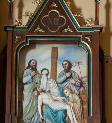 Zdjęcie nr 12: Stacje drogi krzyżowej wkomponowane w rozbudowane, drewniane neogotyckie ramy o formach przypominających kapliczki, flankowane uszakami w kształcie przypór oraz zwieńczone parami pinakli i wimpergą dekorowaną żabkami i zakończoną kwiatonem z krzyżem. Wpisano w nie motyw czworoliścia otoczony trzema rozetkami. Od dołu dekoracyjne podwieszenie. Poszczególne przedstawienia umieszczone za szybą, ujętą w profilowane obramienie w kształcie stojącego prostokąta zamkniętego łukiem nadwieszonym. Sceny są płaskorzeźbione w głębokim reliefie i ukazane na malowanym tle. Dominują zwarte, wielopostaciowe kompozycje o ekspresji wyrażonej zarówno w gestach postaci, jak i mimice twarzy. Kolorystyka pastelowa, dominują odcienie brązu, bieli i niebieskiego ożywione akcentami intensywnej czerwieni płaszcza Chrystusa. W tle fragmenty zabudowań oraz niebo, przybierające barwę od jasnego błękitu po intensywnie niebieski. W czworoliściu wimpergi numery stacji wyrażone cyframi rzymskimi, w dolnej partii obramienia prostokątne płyciny z nazwami stacji:
„I : P(an) Jezus przez Piłata na śmierć skazany”,
„II: P(an) Jezus obciążony krzyżem”, „III: P(an) Jezus upada pierwszy raz”, „IV: P(an) Jezus spotyka swą Matkę”, „V: P(an) Jezusowi dopomaga Szymon Cyre”, „VI: P(an) Jezusowi ociera twarz S. Weronika”, „VII: P(an) Jezus upada drugi raz”, „VIII: P(an) Jezus pociesza płaczące niewiasty”, „IX: P(an) Jezus upada po raz trzeci”, „X: P(an) Jezus obnażony żółcią napawany”, „XI: P(an) Jezus do krzyża przybijany”, „XII: P(an) Jezus umiera na krzyżu”, „XIII: P(an) Jezus zdjęty z krzyża”
„XIV: P(an) Jezus złożony w grobie”. 
