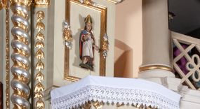 Zdjęcie nr 1: Ambona przyścienna, wisząca, z dostępem od zakrystii. Kosz na rzucie prostokąta z wypukłą ścianką frontową, z dodatkowym podestem od strony prezbiterium, ustawiony na niewielkiej podstawie dekorowanej muszlą, z podwieszeniem w formie zwężającego się cokołu ozdobionego ornamentem roślinnym, zakończonym szyszką. Ścianki kosza dekorowane płycinami w kształcie kwadratu o wklęsłych narożach wypełnionymi dekoracją złożoną z akantu, rozet i kratki regencyjnej. Naroża ścianki przedniej zdobione zwisami utworzonymi z wstęgi i kratki regencyjnej oraz ornamentu roślinnego. Parapet w formie gzymsu. Zaplecek w kształcie pionowego prostokąta, dekorowany w polu profilowaną płyciną z ornamentem roślinnym i płaskorzeźbioną figurą św. Stanisława. Baldachim powtarzający plan kosza, ujęty niepełnym belkowaniem, dekorowanym z trzech stron szczytami, z fragmentami zwróconego na zewnątrz przerwanego, wolutowego przyczółka, stanowiący podstawę dla figury anioła. Na podniebieniu baldachimu gołębica Ducha Świętego w glorii promienistej. Struktura polichromowana w kolorze jasnozielonym ze złoconymi i srebrzonymi profilami oraz ornamentyką. 
Figura anioła pełnoplastyczna, zwrócona jest w trzech czwartych w prawo, w silnym kontrapoście, o esowato wygiętej sylwetce, z głową skierowaną w górę. Obiema rękami obejmuje trąbę, na której gra. Twarz ma pociągłą, o dużych oczach skierowanych w górę, zadartym nosie i pełnych ustach, okoloną silnie kręconymi włosami. Anioł ubrany jest w zapinaną z przodu na guziki, obcisłą kamizelkę z bufiastymi, krótkimi rękawami i wysokim kołnierzem, w pludry i pończochy, wokół bioder ma zawieszony płaszcz, podwiązany po bokach. Skrzydła duże, złożone po bokach postaci. Polichromia ciała naturalistyczna, strój złocony, ze srebrzonymi detalami. 
Po wewnętrznej stronie fragmentu lewego przerwanego przyczółka napis: „odnowiono 1841. / ołtarze 3. tęcę i ambonę / przez Malarza z Tar/nawy Andrzeja / Wierzch[…]”.