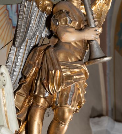 Zdjęcie nr 11: Ambona przyścienna, wisząca, z dostępem od zakrystii. Kosz na rzucie prostokąta z wypukłą ścianką frontową, z dodatkowym podestem od strony prezbiterium, ustawiony na niewielkiej podstawie dekorowanej muszlą, z podwieszeniem w formie zwężającego się cokołu ozdobionego ornamentem roślinnym, zakończonym szyszką. Ścianki kosza dekorowane płycinami w kształcie kwadratu o wklęsłych narożach wypełnionymi dekoracją złożoną z akantu, rozet i kratki regencyjnej. Naroża ścianki przedniej zdobione zwisami utworzonymi z wstęgi i kratki regencyjnej oraz ornamentu roślinnego. Parapet w formie gzymsu. Zaplecek w kształcie pionowego prostokąta, dekorowany w polu profilowaną płyciną z ornamentem roślinnym i płaskorzeźbioną figurą św. Stanisława. Baldachim powtarzający plan kosza, ujęty niepełnym belkowaniem, dekorowanym z trzech stron szczytami, z fragmentami zwróconego na zewnątrz przerwanego, wolutowego przyczółka, stanowiący podstawę dla figury anioła. Na podniebieniu baldachimu gołębica Ducha Świętego w glorii promienistej. Struktura polichromowana w kolorze jasnozielonym ze złoconymi i srebrzonymi profilami oraz ornamentyką. 
Figura anioła pełnoplastyczna, zwrócona jest w trzech czwartych w prawo, w silnym kontrapoście, o esowato wygiętej sylwetce, z głową skierowaną w górę. Obiema rękami obejmuje trąbę, na której gra. Twarz ma pociągłą, o dużych oczach skierowanych w górę, zadartym nosie i pełnych ustach, okoloną silnie kręconymi włosami. Anioł ubrany jest w zapinaną z przodu na guziki, obcisłą kamizelkę z bufiastymi, krótkimi rękawami i wysokim kołnierzem, w pludry i pończochy, wokół bioder ma zawieszony płaszcz, podwiązany po bokach. Skrzydła duże, złożone po bokach postaci. Polichromia ciała naturalistyczna, strój złocony, ze srebrzonymi detalami. 
Po wewnętrznej stronie fragmentu lewego przerwanego przyczółka napis: „odnowiono 1841. / ołtarze 3. tęcę i ambonę / przez Malarza z Tar/nawy Andrzeja / Wierzch[…]”.