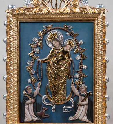 Zdjęcie nr 2: Feretron w formie stojącego prostokąta ujętego ramą, ustawiony na podstawie zamkniętej gzymsem z prostokątnymi otworami na drążki, dekorowanej w narożach czterema uskrzydlonymi główkami anielskimi oraz dwiema girlandami. Rama ozdobiona perełkowaniem, kimationem oraz z trzech stron laurem z rozetami, zwieńczona ażurowym szczytem z monogramem Marii, zamkniętym koroną otwartą, ujętym liśćmi, wolutami, akantem i winnym gronem. 
Na awersie malowane na płótnie przedstawienie Matki Boskiej z Dzieciątkiem przekazującej różaniec św. Dominikowi. W prawym dolnym rogu klęczący św. Dominik, zwrócony w trzech czwartych w prawo, z głową skierowaną w górę. Lewą rękę kładzie na piersi, prawą wyciąga przed siebie. Twarz ma szczupłą, o starczych rysach, z oczami skierowanymi do góry, garbatym nosem i rozchylonymi ustach, okoloną siwą, gęstą brodą i włosami. Ubrany jest w biały habit ze szkaplerzem i różańcem zawieszonym przy boku oraz czarny płaszcz z kapturem. Przy jego lewym boku leży pies z pochodnią w pysku. W górnym lewym rogu obrazu Matka Boska z Dzieciątkiem siedząca na obłoku, zwrócona w trzech czwartych w lewo. Prawą ręką podtrzymuje Dzieciątko, lewą wyciąga przed siebie podając Dominikowi różaniec. Twarz o delikatnych rysach, okolona jasnymi włosami, schowanymi pod welonem. Ubrana jest w czerwoną suknię i niebieski płaszcz opadający na kolana, na głowie ma biały welon. Dzieciątko siedzące na kolanach Marii, prawą rączką trzyma różaniec i podaje go Dominikowi. Twarz ma pełną, okoloną jasnymi włosami, ubrane jest w białą tunikę. Przedstawienie ukazane na tle pejzażu z widocznym kościołem Dominikanów pw. Trójcy Świętej w Krakowie. W górnej części obrazu zachmurzone niebo, rozświetlone wokół postaci Marii z trzema uskrzydlonymi główkami anielskimi. 
Na rewersie płaskorzeźbione przedstawienie Matki Boskiej z Dzieciątkiem, którzy przekazują różańce św. Dominikowi i św. Katarzynie Sieneńskiej. W centrum Maria ukazana w całej postaci, zwrócona frontalnie, z głową pochyloną w prawo, stoi na globie i na półksiężycu, wokół którego wije się wąż gryzący owoc. Lewą ręką podtrzymuje Dzieciątko, prawą podaje różaniec Dominikowi. Twarz ma pociągłą, o łagodnych rysach, oczach skierowanych w dół, okoloną falowanymi włosami. Ubrana jest w złoconą suknię o kwiecistym wzorze i analogiczny płaszcz, na głowie ma koronę zamkniętą. Dzieciątko w pozycji siedzącej, zwrócone w trzech czwartych w prawo, z pochyloną głową skierowaną w lewo. Lewą ręką podaje różaniec Katarzynie, prawą unosi w geście błogosławieństwa. Ubrane jest w złoconą tunikę, przepasaną w talii, na głowie ma koronę zamkniętą. Postać Marii ujęta jest wieńcem z paciorków przeplatanych wicią roślinną z kwiatami. Po jej prawej stronie klęczący św. Dominik, ukazany z profilu, lewą rękę wyciąga po różaniec, prawą przyciska do piersi gałązkę. Ubrany jest w biały habit i czarny płaszcz z kapturem, na głowie ma tonsurę. Przy jego lewym boku leży pies z pochodnią w pysku. Po lewej stronie Marii klęczy św. Katarzyna Sieneńska, zwrócona w trzech czwartych, z prawą ręką sięgającą po różaniec, lewą podtrzymuje na ramieniu krzyż. Jej twarz okalają długie, brązowe włosy, na głowie ma koronę cierniową. Ubrana jest w biały habit i czarny płaszcz. Postacie ukazane są na niebieskim, jednolitym tle, za postaciami świętych malowana trawa.