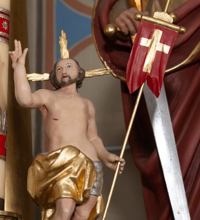 Zdjęcie nr 1: Rzeźba pełnoplastyczna, ustawiona na prostej podstawie o nieregularnym kształcie oraz na niewielkim, rzeźbionym fragmencie skały. Chrystus zwrócony jest frontalnie, z uniesioną głową, skierowaną w prawo, stoi w kontrapoście z wypchniętym w bok lewym biodrem i wysuniętą do przodu prawą nogą. W lewej ręce trzyma drzewce zakończone krzyżem z czerwoną chorągwią ze złoconym krzyżem, prawą unosi w geście błogosławieństwa. Twarz ma kwadratową o wysokim czole, dużych oczach skierowanych do góry, krótkim nosie i pełnych ustach, okoloną krótką brodą oraz kręconymi włosami opadającymi na plecy. Z jego głowy wychodzą trzy wiązki złoconych promieni. Ciało ma szczupłe o delikatnym modelunku mięśni, z zaznaczonymi śladami męki. Biodra przewiązane są ściśle przylegającym, srebrzonym perizonium oraz złoconym płaszczem zarzuconym na prawą nogę i opadającym z tyłu postaci. Między stopami Chrystusa wije się wąż. Polichromia ciała naturalistyczna. 

