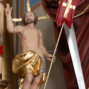 Zdjęcie nr 1: Rzeźba pełnoplastyczna, ustawiona na prostej podstawie o nieregularnym kształcie oraz na niewielkim, rzeźbionym fragmencie skały. Chrystus zwrócony jest frontalnie, z uniesioną głową, skierowaną w prawo, stoi w kontrapoście z wypchniętym w bok lewym biodrem i wysuniętą do przodu prawą nogą. W lewej ręce trzyma drzewce zakończone krzyżem z czerwoną chorągwią ze złoconym krzyżem, prawą unosi w geście błogosławieństwa. Twarz ma kwadratową o wysokim czole, dużych oczach skierowanych do góry, krótkim nosie i pełnych ustach, okoloną krótką brodą oraz kręconymi włosami opadającymi na plecy. Z jego głowy wychodzą trzy wiązki złoconych promieni. Ciało ma szczupłe o delikatnym modelunku mięśni, z zaznaczonymi śladami męki. Biodra przewiązane są ściśle przylegającym, srebrzonym perizonium oraz złoconym płaszczem zarzuconym na prawą nogę i opadającym z tyłu postaci. Między stopami Chrystusa wije się wąż. Polichromia ciała naturalistyczna. 

