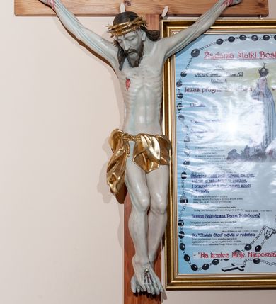 Zdjęcie nr 1: Figura umarłego Chrystusa przybita jest do krzyża o prostym zakończeniu ramion trzema gwoździami. Ciało w dużym zwisie, o układzie ramion przypominającym literę „V”, głowa opada na prawy bark, stopy skrzyżowane są w układzie prawa na lewą. Chrystus ma szczupłą i pociągłą twarz, o zamkniętych oczach, prostym, długim nosie i rozchylonych, szerokich ustach, okoloną brodą i włosami sięgającymi ramion. Na głowie ma złoconą koronę cierniową. Jego ciało jest bardzo szczupłe z podkreślonymi mięśniami i ścięgnami nóg i użyleniem ramion oraz żebrami klatki piersiowej. Perizonium złocone, krótkie, zawieszone na podwójnym sznurze, odsłaniające prawe udo, ze zwisem tkaniny wzdłuż prawej nogi. Polichromia ciała naturalistyczna, z podkreśleniem bladej karnacji i z zaznaczonymi śladami męki. Na zakończeniu pionowej belki krzyża srebrzona banderola z napisem „IESU(S) NAZ[A]/RENUS REX / JVD(A)EORUM”. 