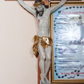 Zdjęcie nr 1: Figura umarłego Chrystusa przybita jest do krzyża o prostym zakończeniu ramion trzema gwoździami. Ciało w dużym zwisie, o układzie ramion przypominającym literę „V”, głowa opada na prawy bark, stopy skrzyżowane są w układzie prawa na lewą. Chrystus ma szczupłą i pociągłą twarz, o zamkniętych oczach, prostym, długim nosie i rozchylonych, szerokich ustach, okoloną brodą i włosami sięgającymi ramion. Na głowie ma złoconą koronę cierniową. Jego ciało jest bardzo szczupłe z podkreślonymi mięśniami i ścięgnami nóg i użyleniem ramion oraz żebrami klatki piersiowej. Perizonium złocone, krótkie, zawieszone na podwójnym sznurze, odsłaniające prawe udo, ze zwisem tkaniny wzdłuż prawej nogi. Polichromia ciała naturalistyczna, z podkreśleniem bladej karnacji i z zaznaczonymi śladami męki. Na zakończeniu pionowej belki krzyża srebrzona banderola z napisem „IESU(S) NAZ[A]/RENUS REX / JVD(A)EORUM”. 