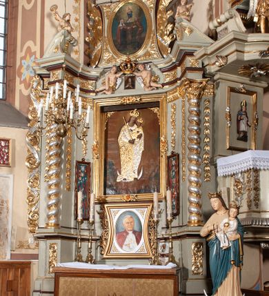 Zdjęcie nr 4: Nastawa architektoniczna, jednoosiowa, jednokondygnacyjna ze zwieńczeniem, ustawiona na cokole z wyodrębnionymi po bokach dwoma postumentami. Ołtarz prostopadłościenny z drewnianą mensą, z portatylem. Antepedium z kwiecistej tkaniny, z wyhaftowanym monogramem Marii w centrum, ujęte profilowaną ramą. Nastawa flankowana parą kolumn o skręconych trzonach i kapitelach kompozytowych stojących na tle dwóch par pilastrów o trzonach dekorowanych kampanulami. Podpory dźwigają pełne belkowanie, wyłamane na ich osi, o wklęsłym zarysie, przerwane nad polem środkowym, z fryzem dekorowanym rozetami oraz fragmenty przerwanego, falistego przyczółka ozdobionego kampanulami z parą puttów z wachlarzami. W polu nisza w formie stojącego prostokąta z obrazem Matki Boskiej Niepokalanie Poczętej w profilowanej ramie, flankowana dwiema gablotami z wotami. Nad polem środkowym dwa putta trzymające koronę zamkniętą oraz ryngraf malowany na blasze z przedstawieniem Matki Boskiej Bolesnej. Nastawa flankowana uszami utworzonymi z akantu i wstęgi regencyjnej. Zwieńczenie w formie stojącego prostokąta, o wklęsłych bokach, zamkniętego odcinkiem gzymsu wyłamanym w łuk ostry, ujęte liśćmi palmowymi z wstęgą. Całość zamknięta medalionem z monogramem Marii, w otoku z obłoków i uskrzydlonych główek anielskich, w glorii promienistej. W polu obraz przedstawiający Rodzinę Marii w formie stojącego owalu, w profilowanej ramie. Pole zwieńczenia wypełnione ornamentem roślinnym. Struktura architektoniczna polichromowana w kolorze jasnozielonym, kolumny, ornamentyka i profile złocone i srebrzone. 