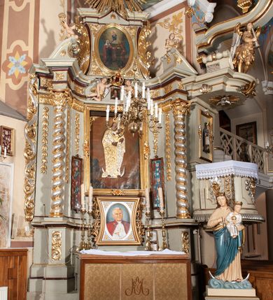 Zdjęcie nr 3: Nastawa architektoniczna, jednoosiowa, jednokondygnacyjna ze zwieńczeniem, ustawiona na cokole z wyodrębnionymi po bokach dwoma postumentami. Ołtarz prostopadłościenny z drewnianą mensą, z portatylem. Antepedium z kwiecistej tkaniny, z wyhaftowanym monogramem Marii w centrum, ujęte profilowaną ramą. Nastawa flankowana parą kolumn o skręconych trzonach i kapitelach kompozytowych stojących na tle dwóch par pilastrów o trzonach dekorowanych kampanulami. Podpory dźwigają pełne belkowanie, wyłamane na ich osi, o wklęsłym zarysie, przerwane nad polem środkowym, z fryzem dekorowanym rozetami oraz fragmenty przerwanego, falistego przyczółka ozdobionego kampanulami z parą puttów z wachlarzami. W polu nisza w formie stojącego prostokąta z obrazem Matki Boskiej Niepokalanie Poczętej w profilowanej ramie, flankowana dwiema gablotami z wotami. Nad polem środkowym dwa putta trzymające koronę zamkniętą oraz ryngraf malowany na blasze z przedstawieniem Matki Boskiej Bolesnej. Nastawa flankowana uszami utworzonymi z akantu i wstęgi regencyjnej. Zwieńczenie w formie stojącego prostokąta, o wklęsłych bokach, zamkniętego odcinkiem gzymsu wyłamanym w łuk ostry, ujęte liśćmi palmowymi z wstęgą. Całość zamknięta medalionem z monogramem Marii, w otoku z obłoków i uskrzydlonych główek anielskich, w glorii promienistej. W polu obraz przedstawiający Rodzinę Marii w formie stojącego owalu, w profilowanej ramie. Pole zwieńczenia wypełnione ornamentem roślinnym. Struktura architektoniczna polichromowana w kolorze jasnozielonym, kolumny, ornamentyka i profile złocone i srebrzone. 