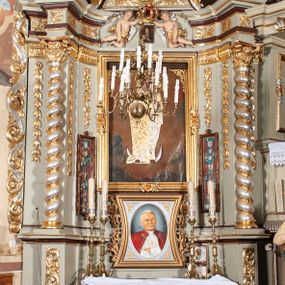 Zdjęcie nr 1: Nastawa architektoniczna, jednoosiowa, jednokondygnacyjna ze zwieńczeniem, ustawiona na cokole z wyodrębnionymi po bokach dwoma postumentami. Ołtarz prostopadłościenny z drewnianą mensą, z portatylem. Antepedium z kwiecistej tkaniny, z wyhaftowanym monogramem Marii w centrum, ujęte profilowaną ramą. Nastawa flankowana parą kolumn o skręconych trzonach i kapitelach kompozytowych stojących na tle dwóch par pilastrów o trzonach dekorowanych kampanulami. Podpory dźwigają pełne belkowanie, wyłamane na ich osi, o wklęsłym zarysie, przerwane nad polem środkowym, z fryzem dekorowanym rozetami oraz fragmenty przerwanego, falistego przyczółka ozdobionego kampanulami z parą puttów z wachlarzami. W polu nisza w formie stojącego prostokąta z obrazem Matki Boskiej Niepokalanie Poczętej w profilowanej ramie, flankowana dwiema gablotami z wotami. Nad polem środkowym dwa putta trzymające koronę zamkniętą oraz ryngraf malowany na blasze z przedstawieniem Matki Boskiej Bolesnej. Nastawa flankowana uszami utworzonymi z akantu i wstęgi regencyjnej. Zwieńczenie w formie stojącego prostokąta, o wklęsłych bokach, zamkniętego odcinkiem gzymsu wyłamanym w łuk ostry, ujęte liśćmi palmowymi z wstęgą. Całość zamknięta medalionem z monogramem Marii, w otoku z obłoków i uskrzydlonych główek anielskich, w glorii promienistej. W polu obraz przedstawiający Rodzinę Marii w formie stojącego owalu, w profilowanej ramie. Pole zwieńczenia wypełnione ornamentem roślinnym. Struktura architektoniczna polichromowana w kolorze jasnozielonym, kolumny, ornamentyka i profile złocone i srebrzone. 