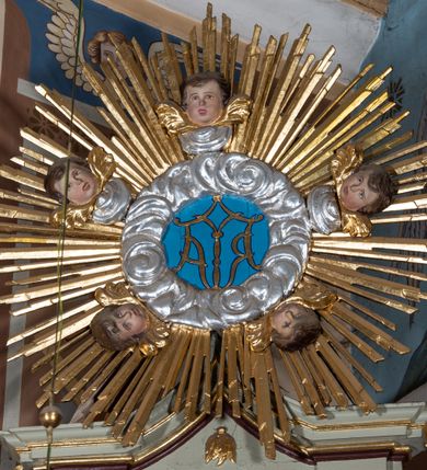 Zdjęcie nr 12: Nastawa architektoniczna, jednoosiowa, jednokondygnacyjna ze zwieńczeniem, ustawiona na cokole z wyodrębnionymi po bokach dwoma postumentami. Ołtarz prostopadłościenny z drewnianą mensą, z portatylem. Antepedium z kwiecistej tkaniny, z wyhaftowanym monogramem Marii w centrum, ujęte profilowaną ramą. Nastawa flankowana parą kolumn o skręconych trzonach i kapitelach kompozytowych stojących na tle dwóch par pilastrów o trzonach dekorowanych kampanulami. Podpory dźwigają pełne belkowanie, wyłamane na ich osi, o wklęsłym zarysie, przerwane nad polem środkowym, z fryzem dekorowanym rozetami oraz fragmenty przerwanego, falistego przyczółka ozdobionego kampanulami z parą puttów z wachlarzami. W polu nisza w formie stojącego prostokąta z obrazem Matki Boskiej Niepokalanie Poczętej w profilowanej ramie, flankowana dwiema gablotami z wotami. Nad polem środkowym dwa putta trzymające koronę zamkniętą oraz ryngraf malowany na blasze z przedstawieniem Matki Boskiej Bolesnej. Nastawa flankowana uszami utworzonymi z akantu i wstęgi regencyjnej. Zwieńczenie w formie stojącego prostokąta, o wklęsłych bokach, zamkniętego odcinkiem gzymsu wyłamanym w łuk ostry, ujęte liśćmi palmowymi z wstęgą. Całość zamknięta medalionem z monogramem Marii, w otoku z obłoków i uskrzydlonych główek anielskich, w glorii promienistej. W polu obraz przedstawiający Rodzinę Marii w formie stojącego owalu, w profilowanej ramie. Pole zwieńczenia wypełnione ornamentem roślinnym. Struktura architektoniczna polichromowana w kolorze jasnozielonym, kolumny, ornamentyka i profile złocone i srebrzone. 